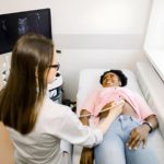 Jeune sage femme française exécutant l’examen de l’abdomen avec le dispositif d’échographie pour son jeune patient féminin africain